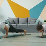 Male and female yoga students are practising downward dog position at home focused on practice on mats, people are moving simultaneously doing asanas.