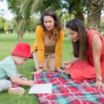A child and two women enjoying a drawing session on a picnic blanket in a park in Portugal.